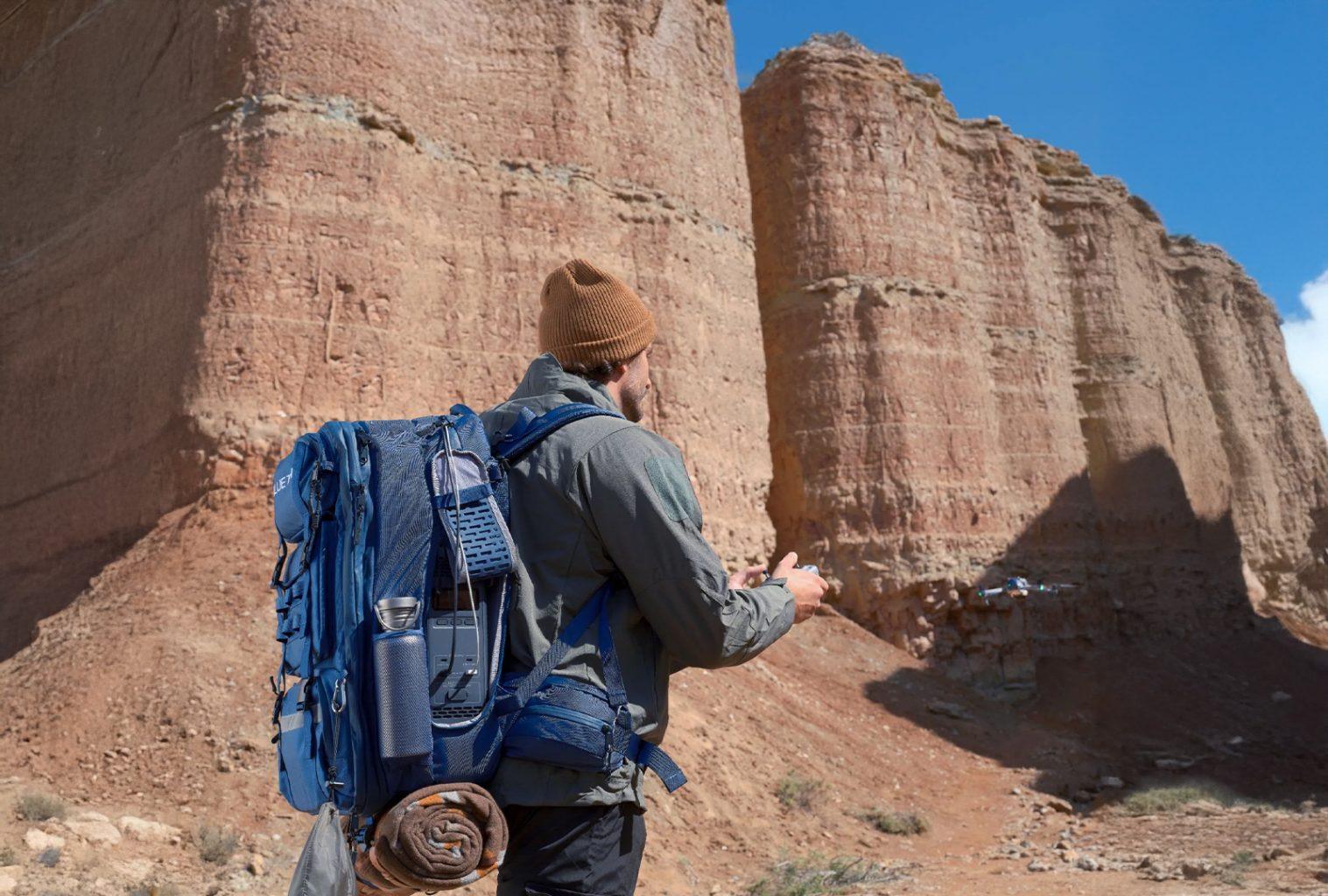 Man flying a drone in the desert with Bluetti hands-free power backpack loaded with gear