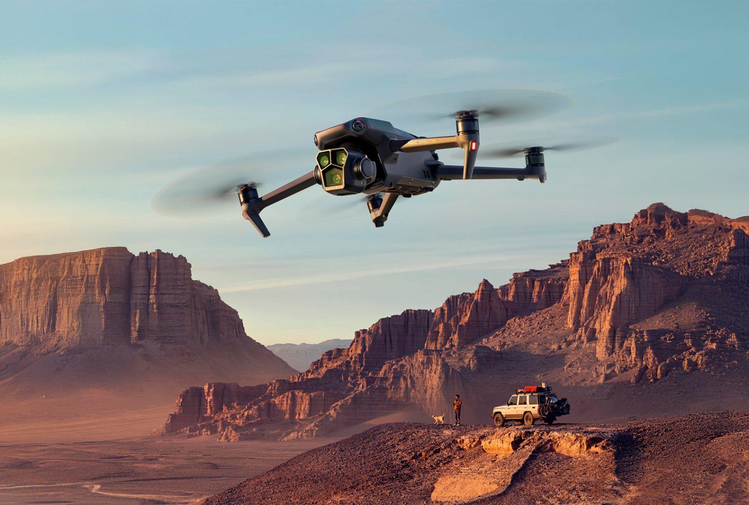 DJI drone flying over remote desert cliffs at sunset with a photographer and 4WD vehicle on the ridge below