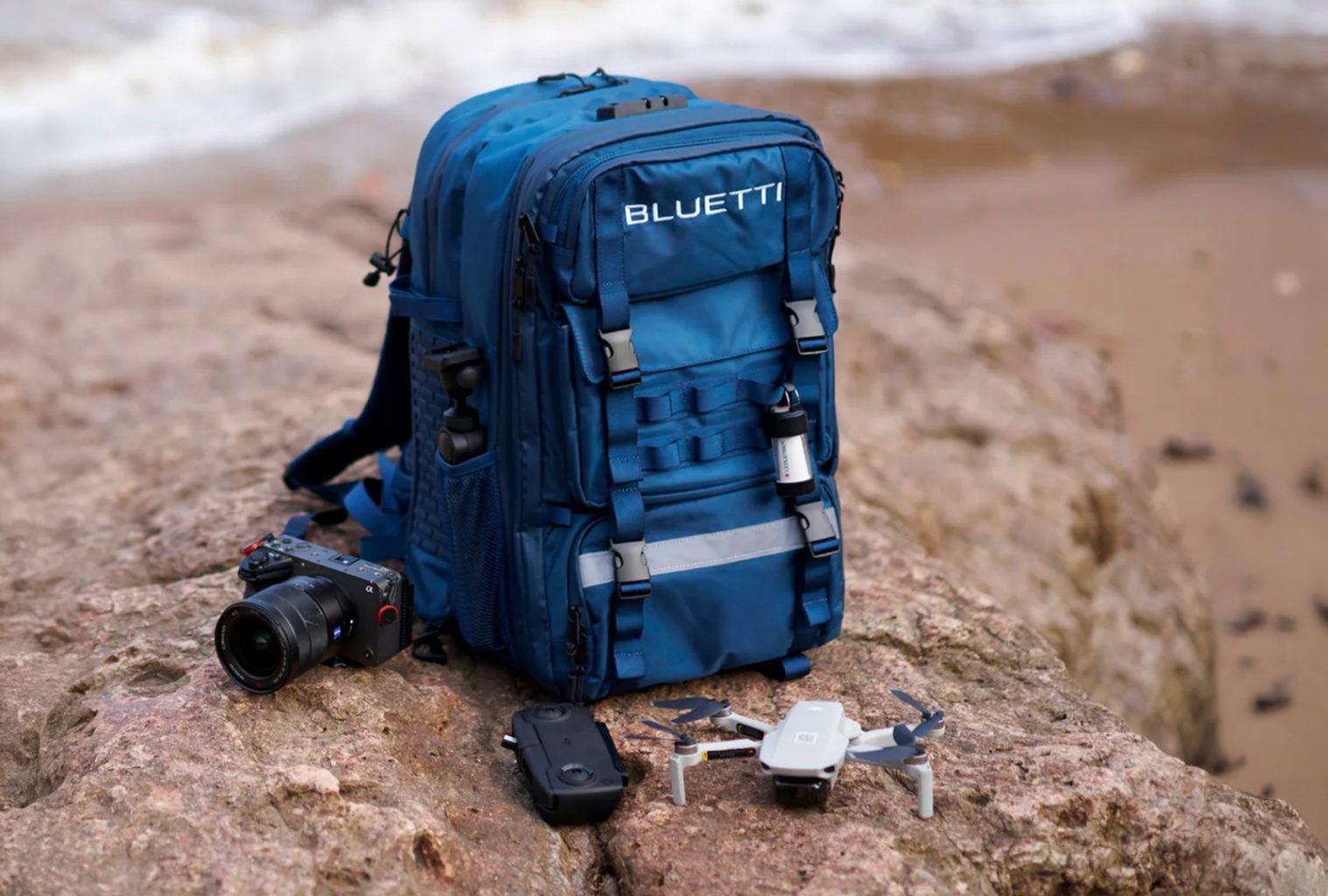 Bluetti hands-free power backpack placed on a coastal rock beside a compact drone, controller, and professional camera