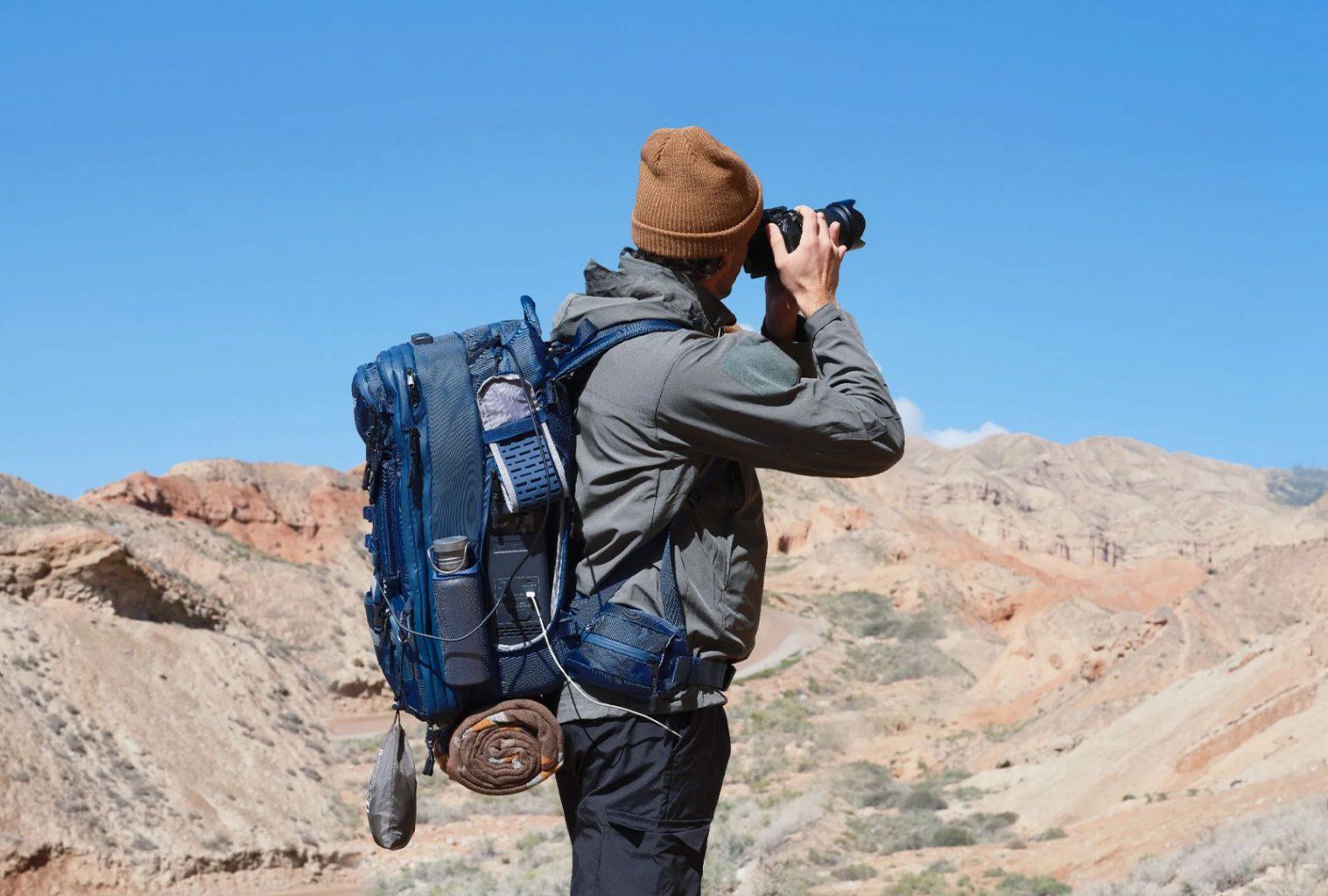 Man photographing desert landscape with professional camera and Bluetti hands-free backpack fully equipped for remote travel