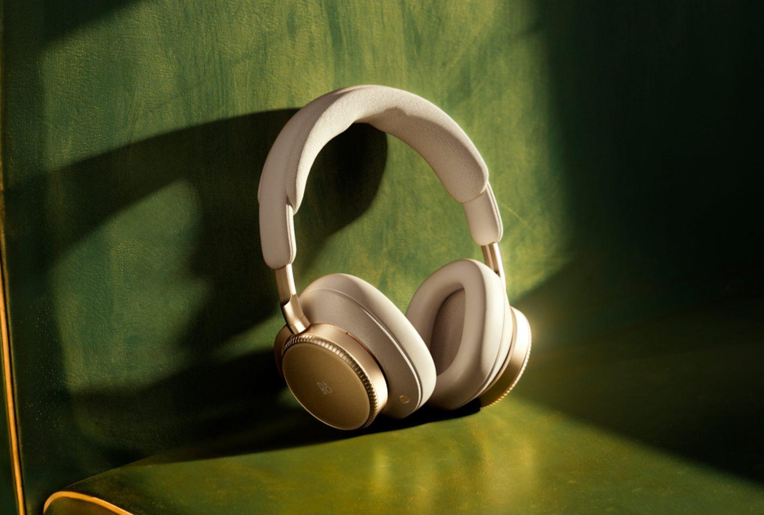 Bang & Olufsen Beoplay H100 headphones resting on a green velvet chair, softly lit in a moody interior setting.