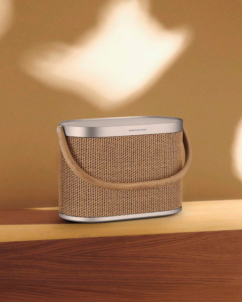 Beosound A5 speaker in Nordic Weave finish on a warm-toned wood table with soft lighting.