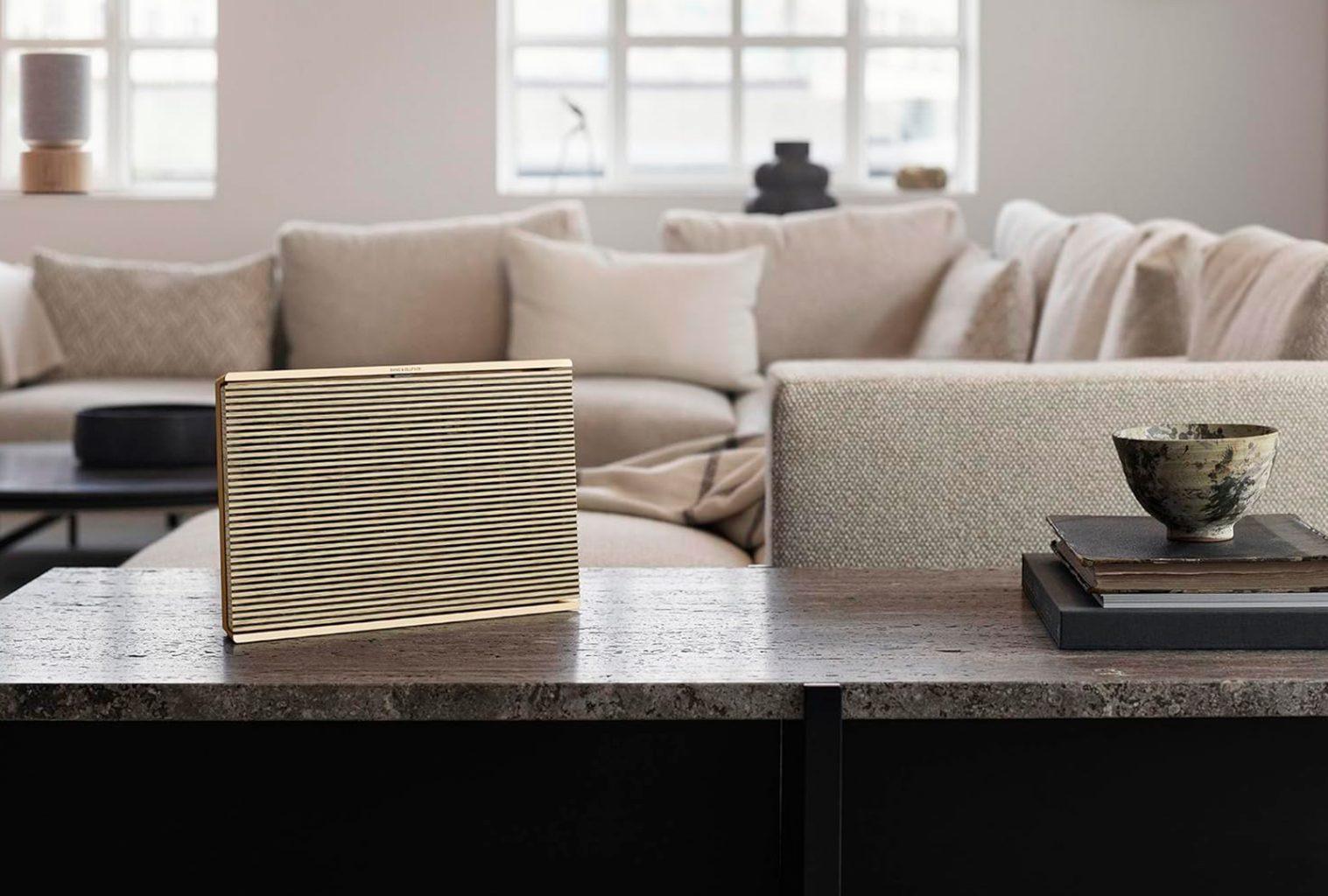 Bang & Olufsen Beosound Level wireless speaker in Gold Tone, placed on a stone benchtop in a bright luxury living room