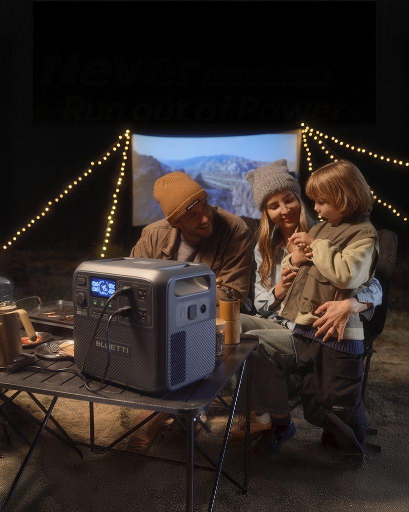 Family camping at night with a Bluetti AC200L power station on a table, illuminating the scene with string lights and a portable projector.