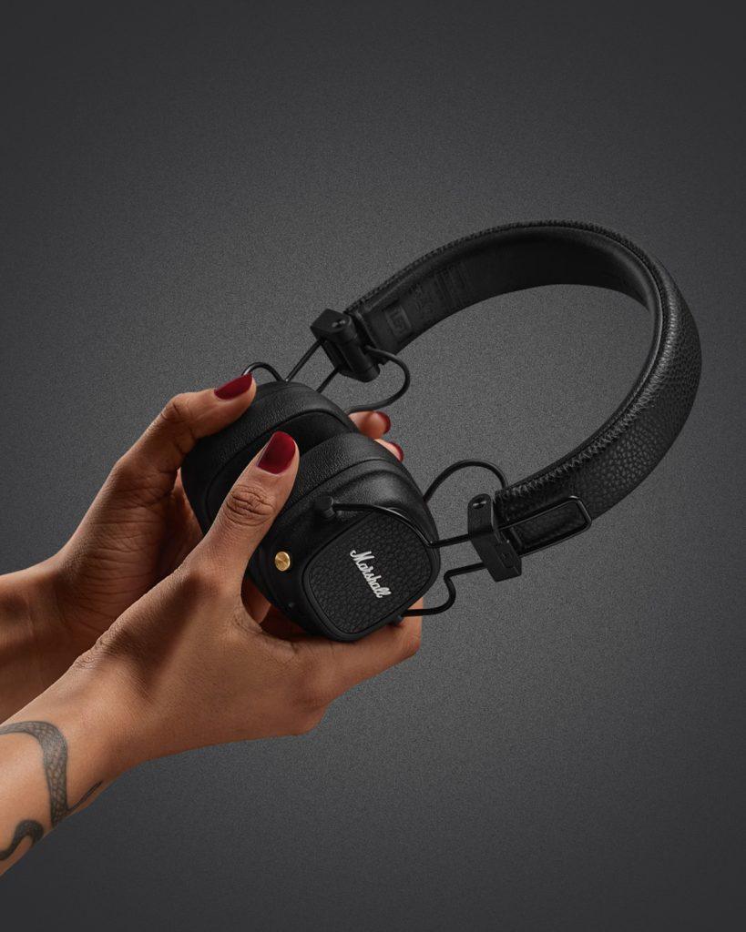 Close-up of hands holding the Marshall Major V headphones in black leather finish, showing foldable design and signature textured ear cups.
