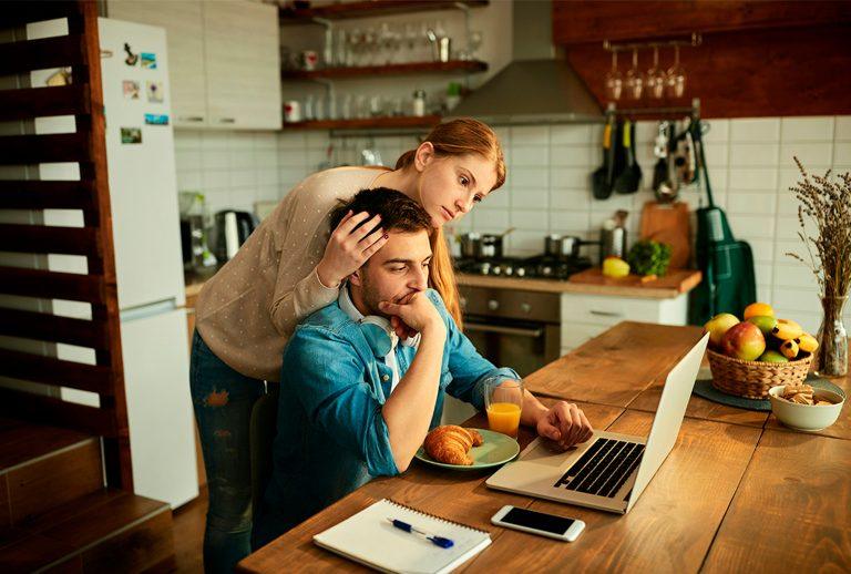 Worried couple in their kitchen looking at a laptop, researching home energy or battery storage options.