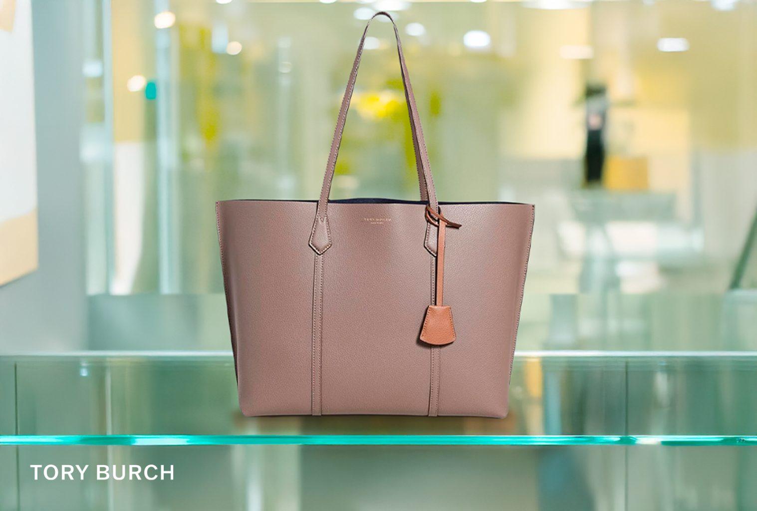 Tory Burch Perry tote in soft taupe leather with top handles, shown on boutique shelf with designer lighting.